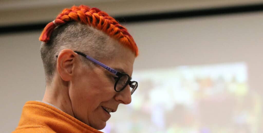 Close-up photo of librarian with short, bright orange hair braided looks down through glasses